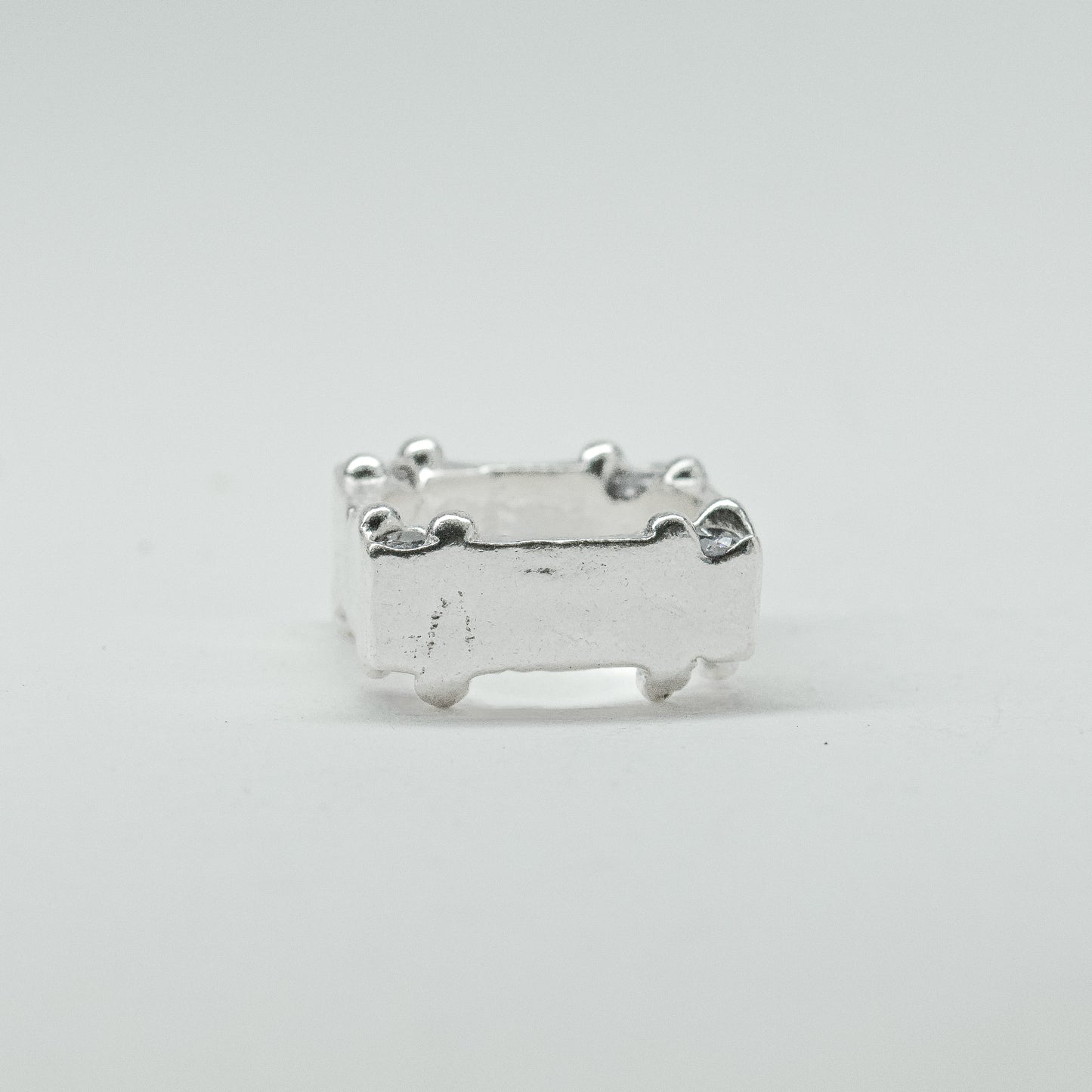 Hand-sculpted sterling silver ring with a bold, square silhouette and deep textured finish, featuring small round gemstones set into each corner.