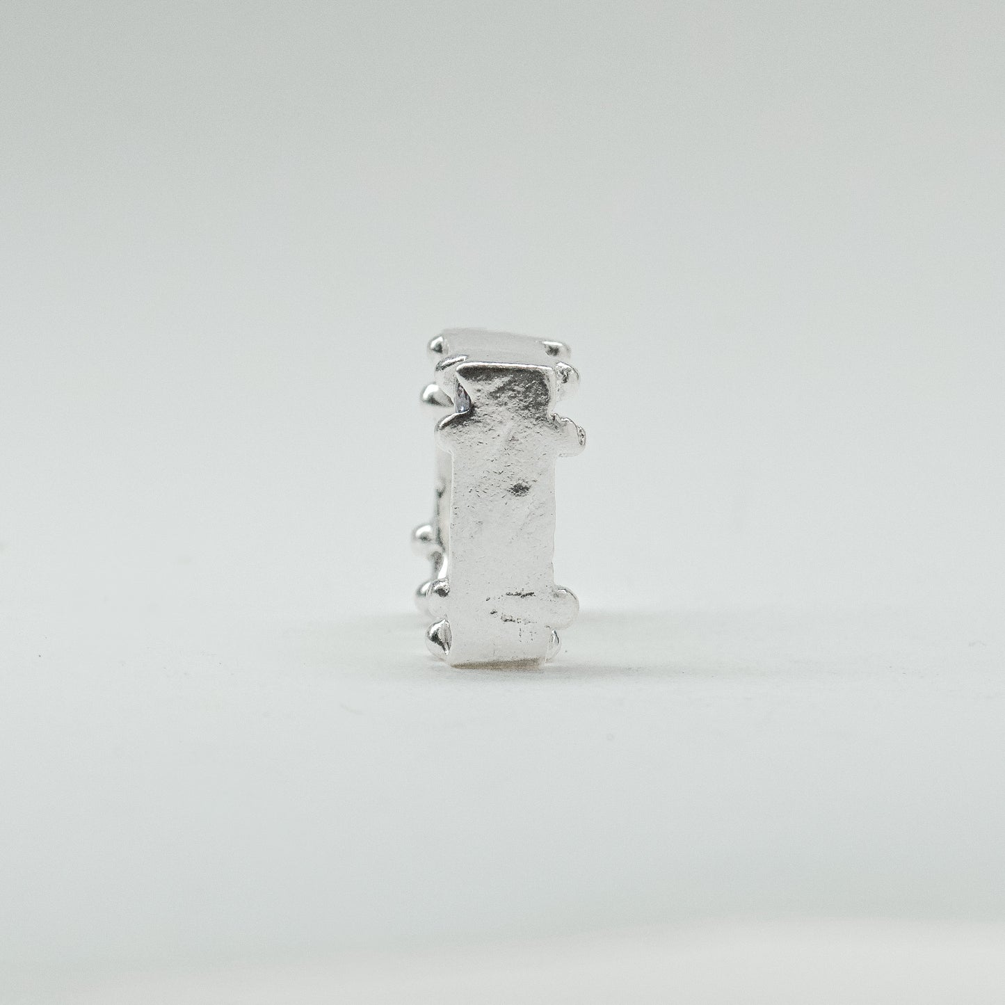 Hand-sculpted sterling silver ring with a bold, square silhouette and deep textured finish, featuring small round gemstones set into each corner.