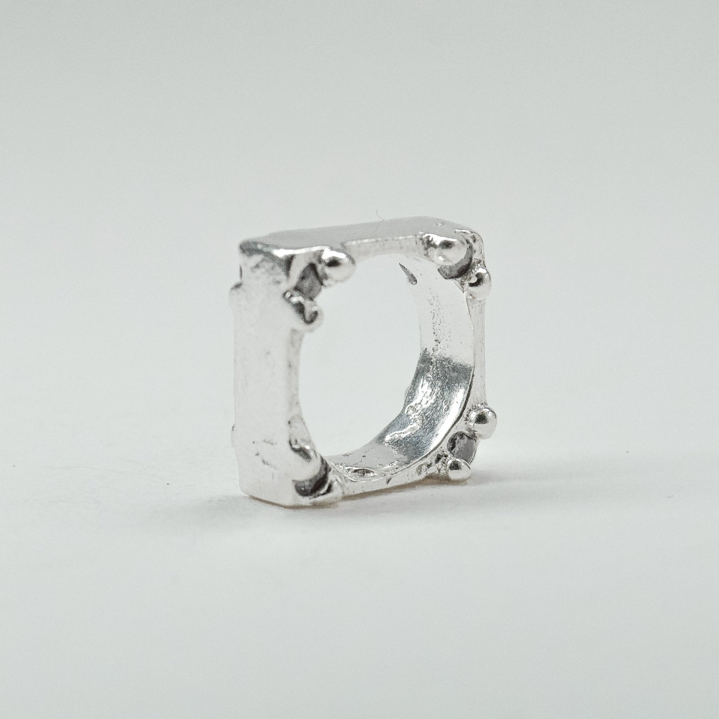 Hand-sculpted sterling silver ring with a bold, square silhouette and deep textured finish, featuring small round gemstones set into each corner.