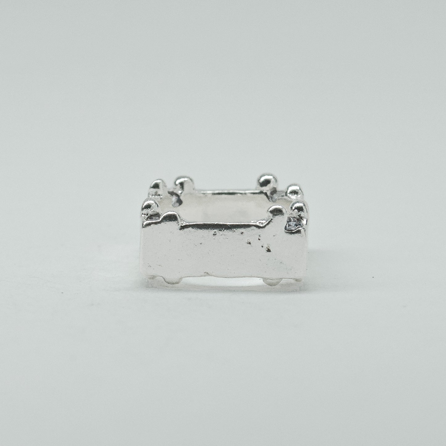 Hand-sculpted sterling silver ring with a bold, square silhouette and deep textured finish, featuring small round gemstones set into each corner.