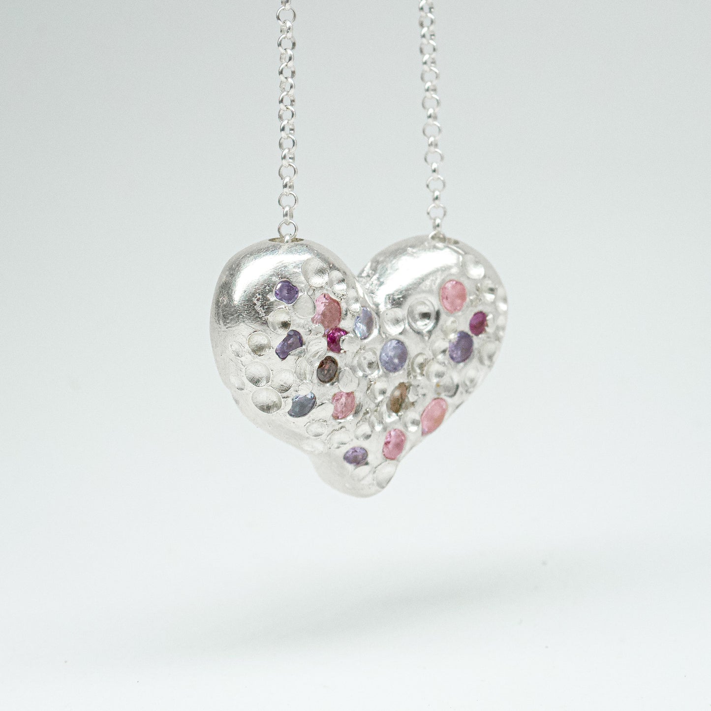 Bulbous heart-shaped sterling silver pendant, hand-sculpted with drilled textures and encrusted with small scattered gemstones. Playful and raw, with a cartoon-like silhouette.
