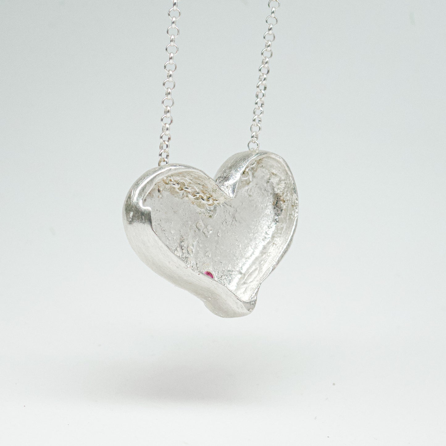 Bulbous heart-shaped sterling silver pendant, hand-sculpted with drilled textures and encrusted with small scattered gemstones. Playful and raw, with a cartoon-like silhouette.