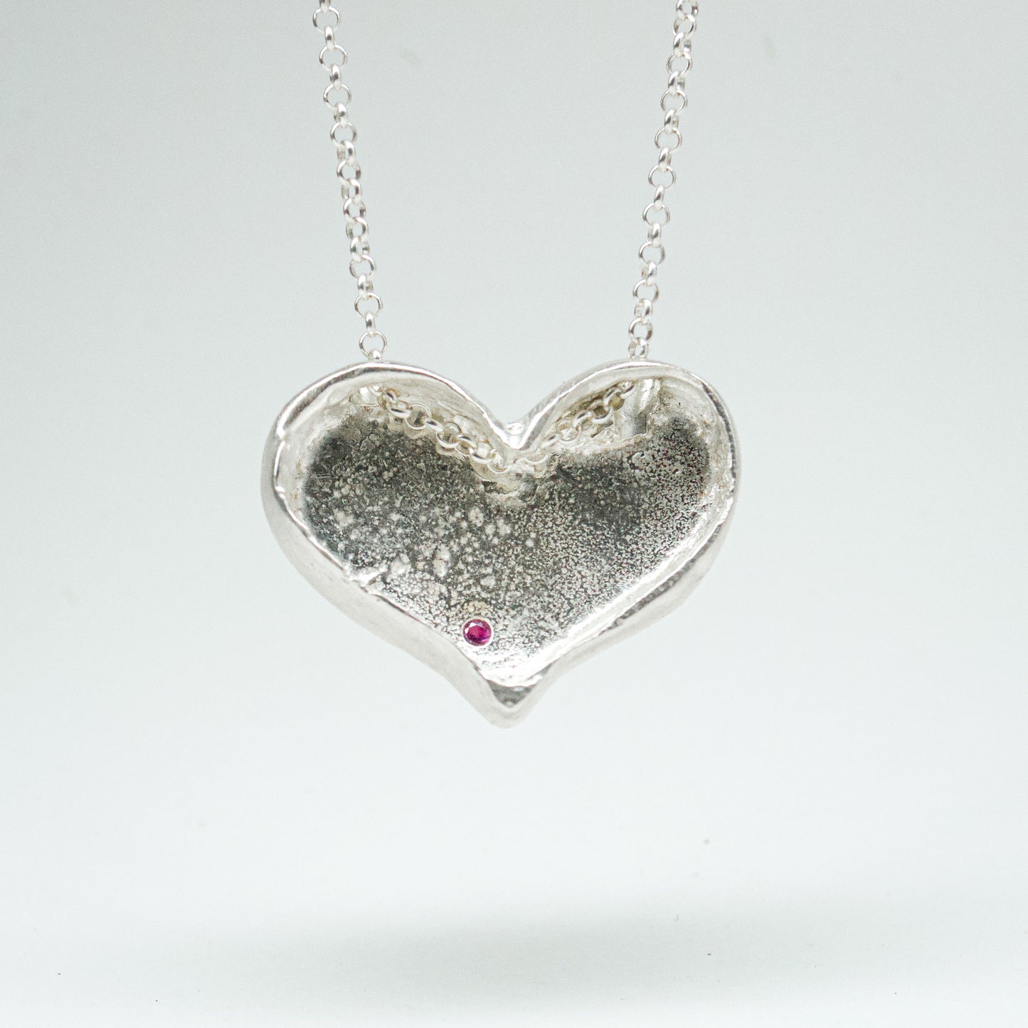 Bulbous heart-shaped sterling silver pendant, hand-sculpted with drilled textures and encrusted with small scattered gemstones. Playful and raw, with a cartoon-like silhouette.
