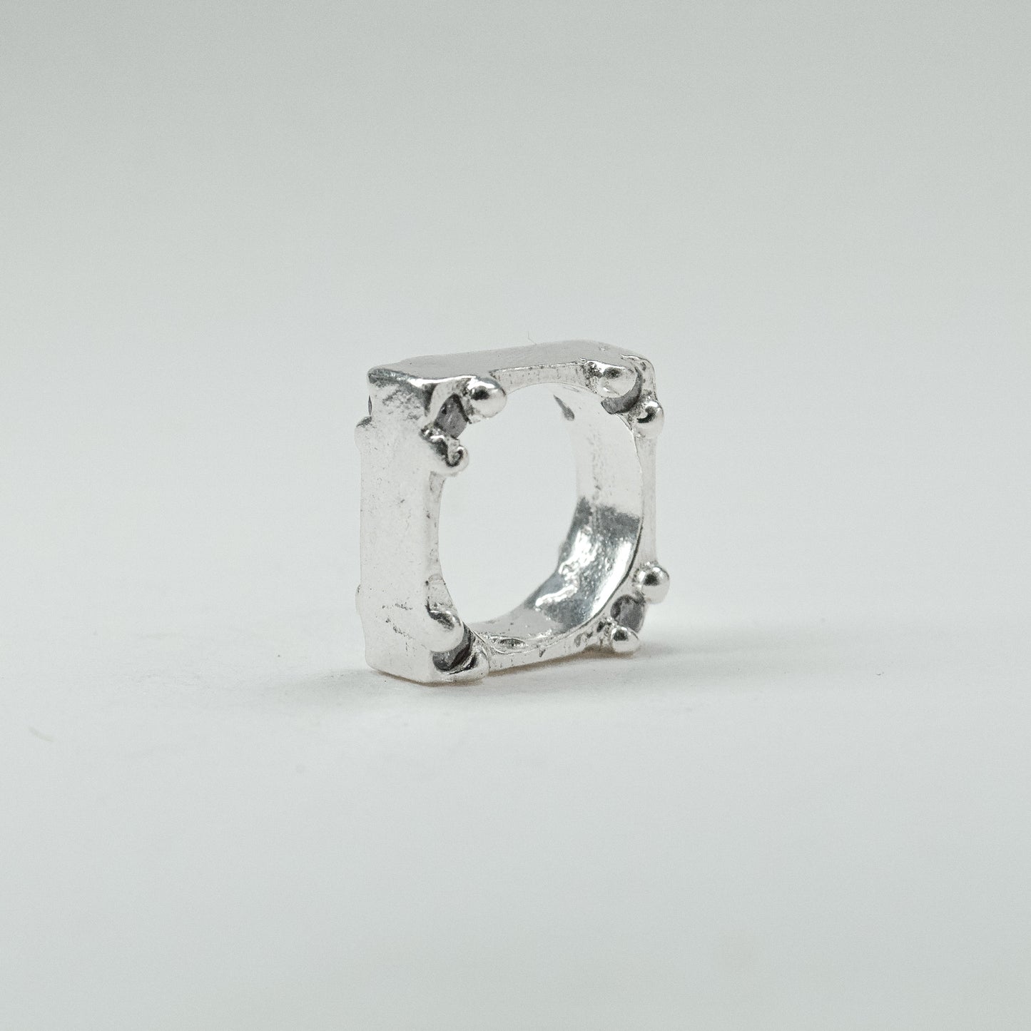 Hand-sculpted sterling silver ring with a bold, square silhouette and deep textured finish, featuring small round gemstones set into each corner.