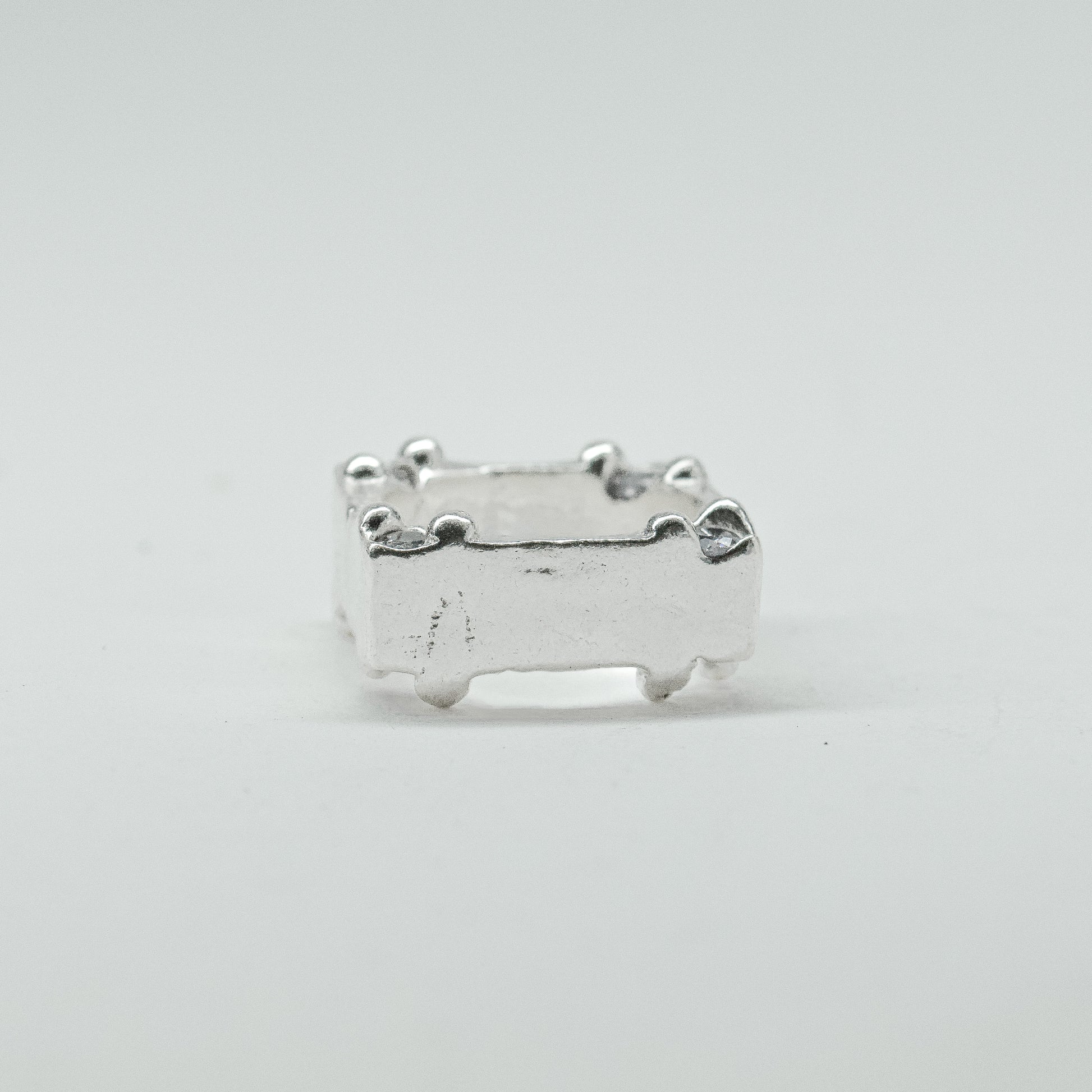 Hand-sculpted sterling silver ring with a bold, square silhouette and deep textured finish, featuring small round gemstones set into each corner.