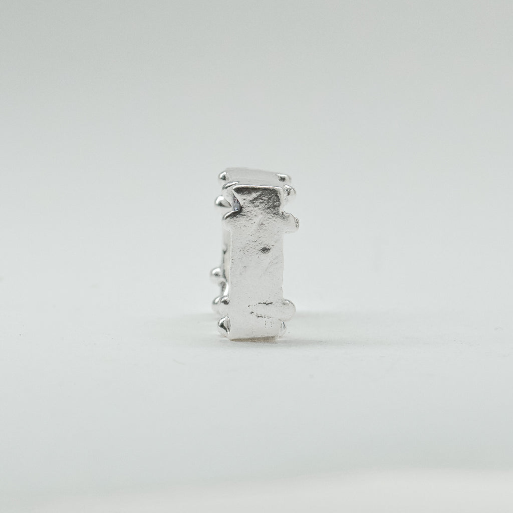 Hand-sculpted sterling silver ring with a bold, square silhouette and deep textured finish, featuring small round gemstones set into each corner.
