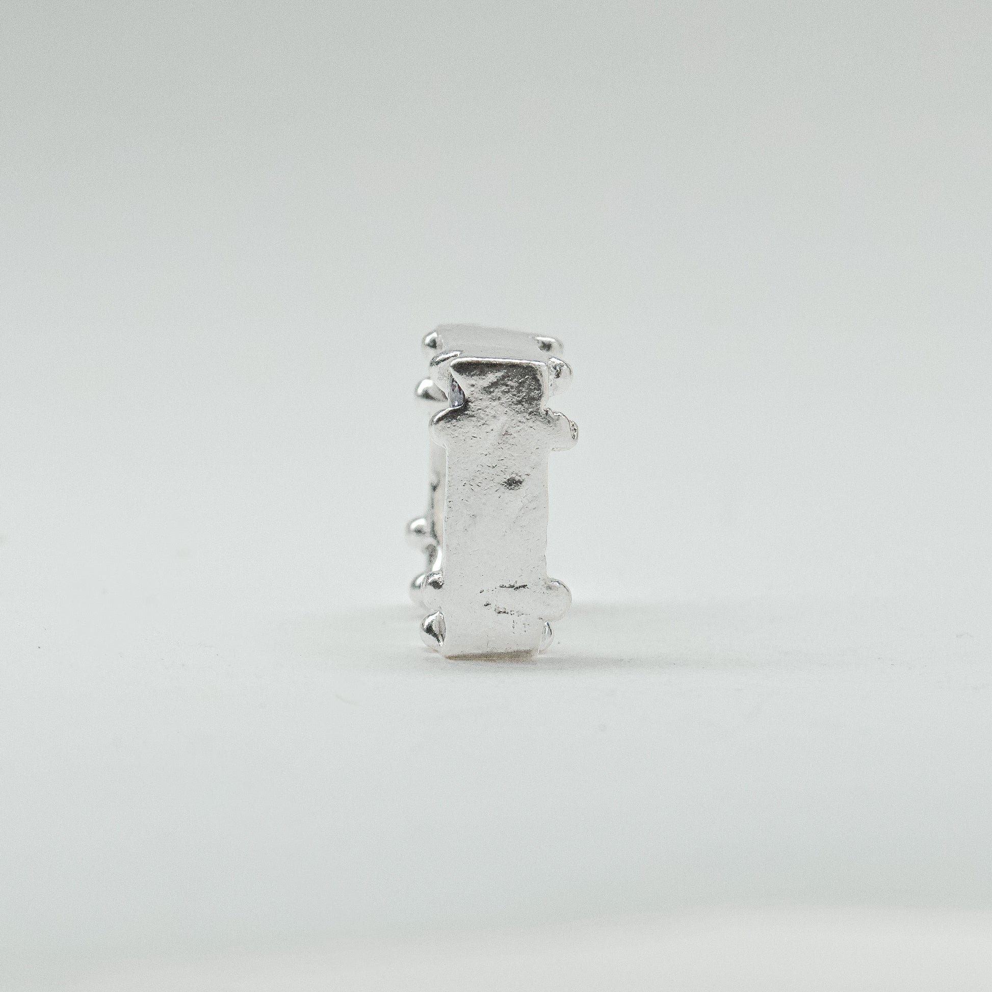 Hand-sculpted sterling silver ring with a bold, square silhouette and deep textured finish, featuring small round gemstones set into each corner.