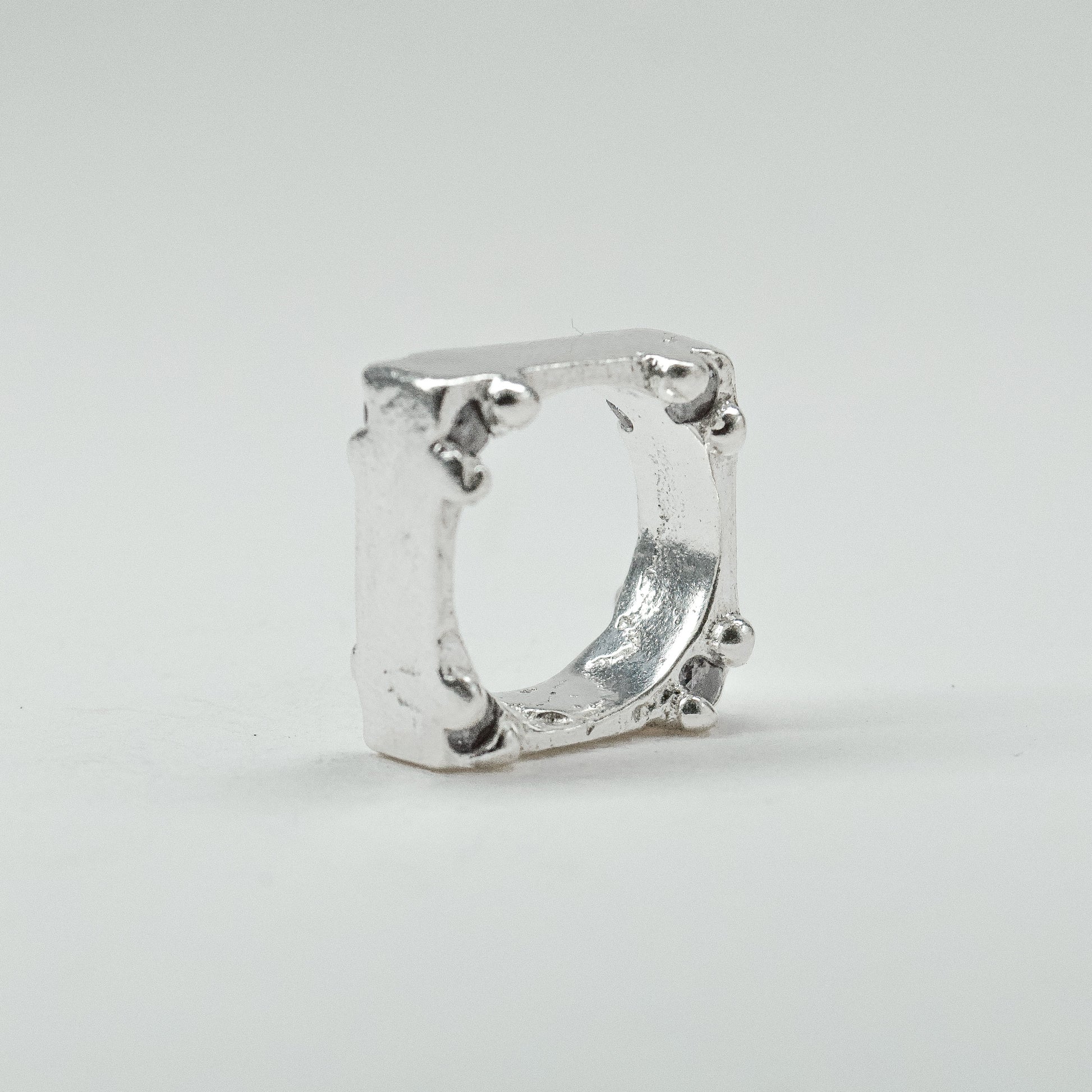 Hand-sculpted sterling silver ring with a bold, square silhouette and deep textured finish, featuring small round gemstones set into each corner.