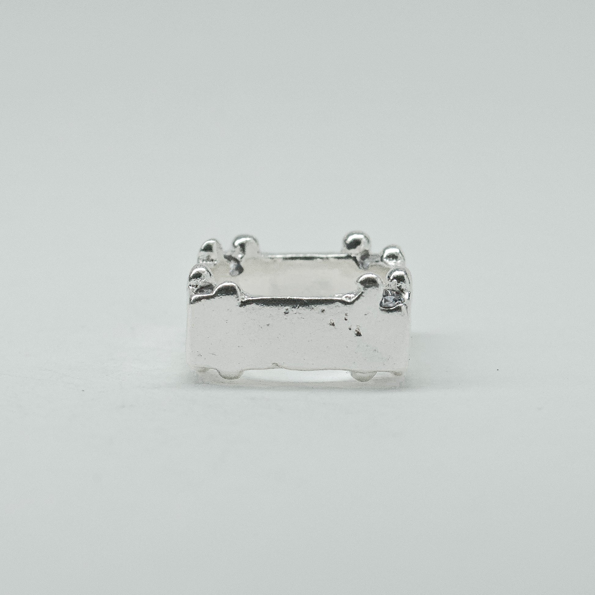 Hand-sculpted sterling silver ring with a bold, square silhouette and deep textured finish, featuring small round gemstones set into each corner.