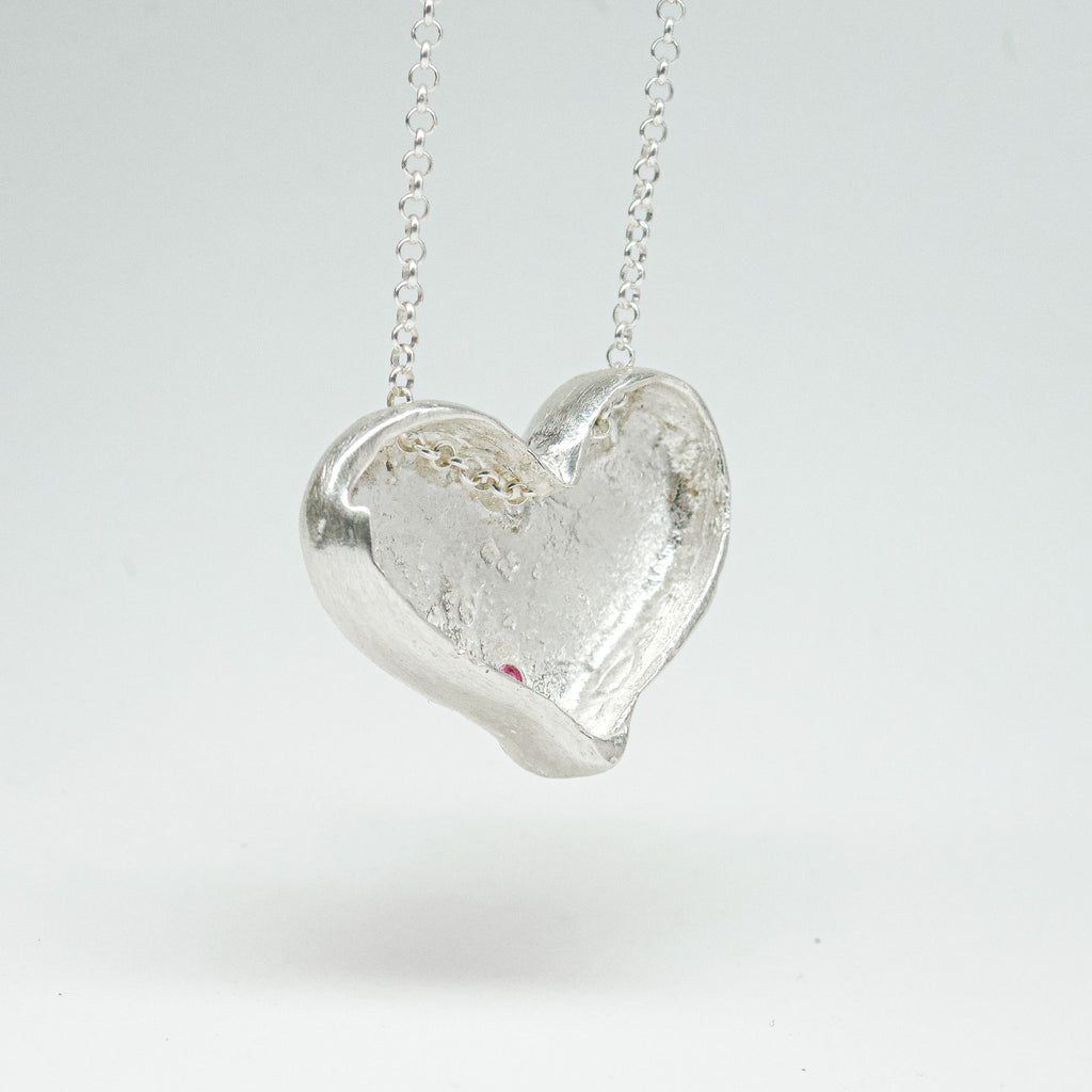 Bulbous heart-shaped sterling silver pendant, hand-sculpted with drilled textures and encrusted with small scattered gemstones. Playful and raw, with a cartoon-like silhouette.