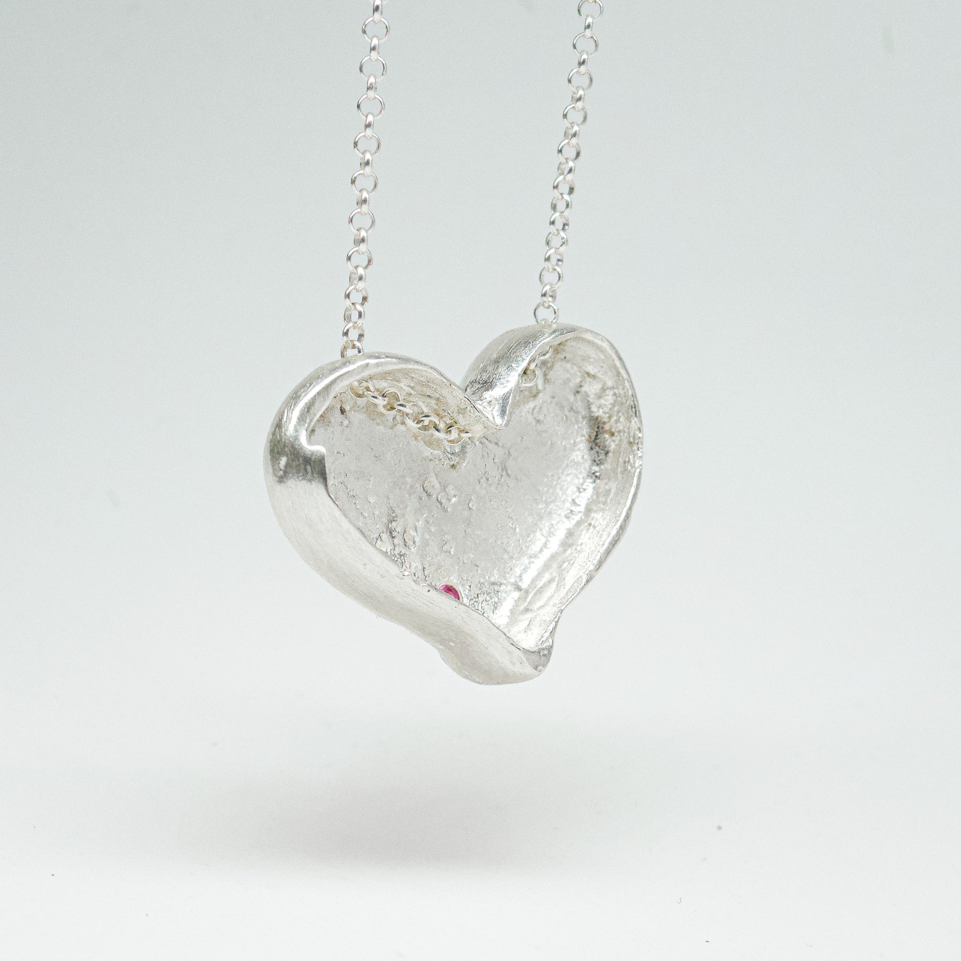Bulbous heart-shaped sterling silver pendant, hand-sculpted with drilled textures and encrusted with small scattered gemstones. Playful and raw, with a cartoon-like silhouette.