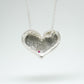 Bulbous heart-shaped sterling silver pendant, hand-sculpted with drilled textures and encrusted with small scattered gemstones. Playful and raw, with a cartoon-like silhouette.