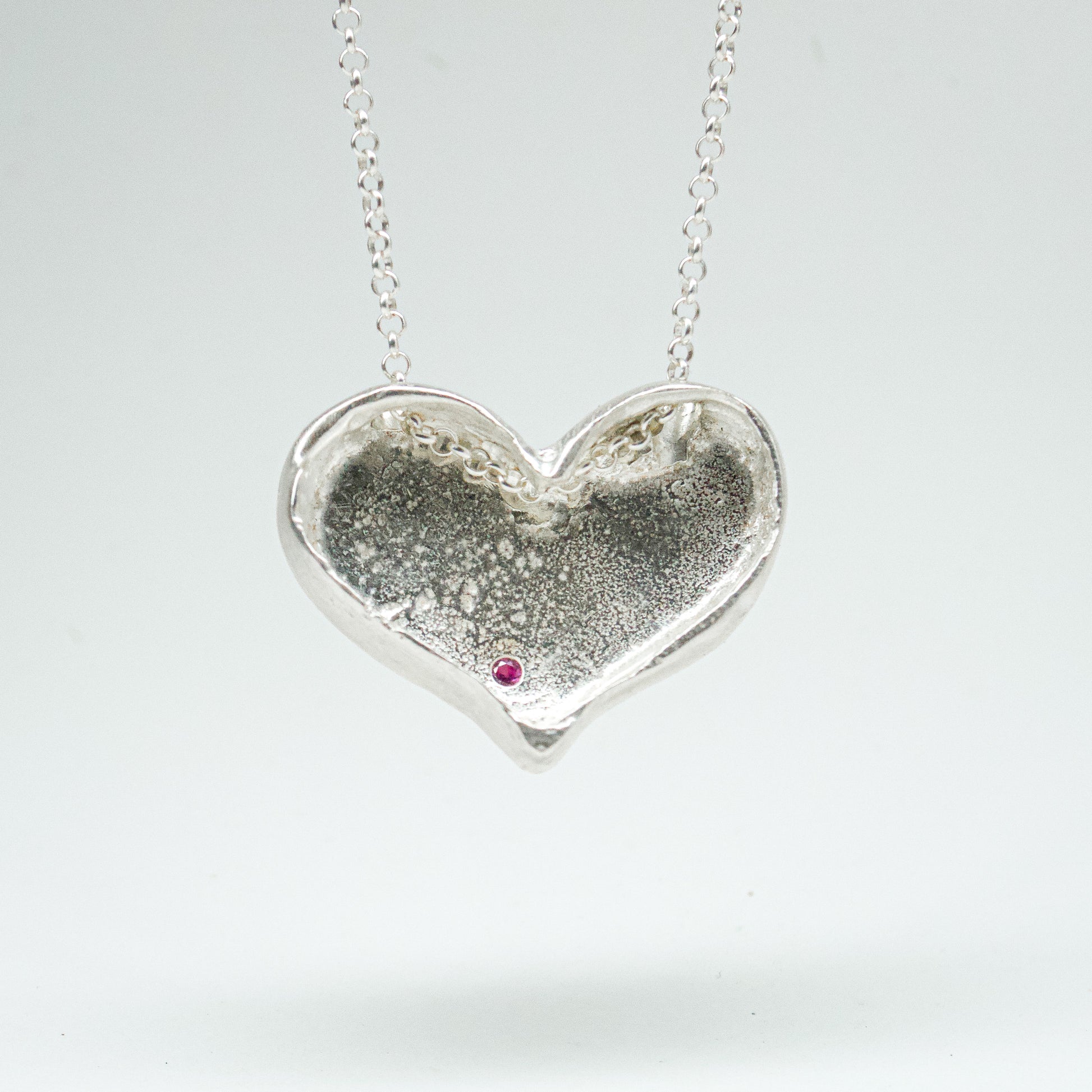Bulbous heart-shaped sterling silver pendant, hand-sculpted with drilled textures and encrusted with small scattered gemstones. Playful and raw, with a cartoon-like silhouette.