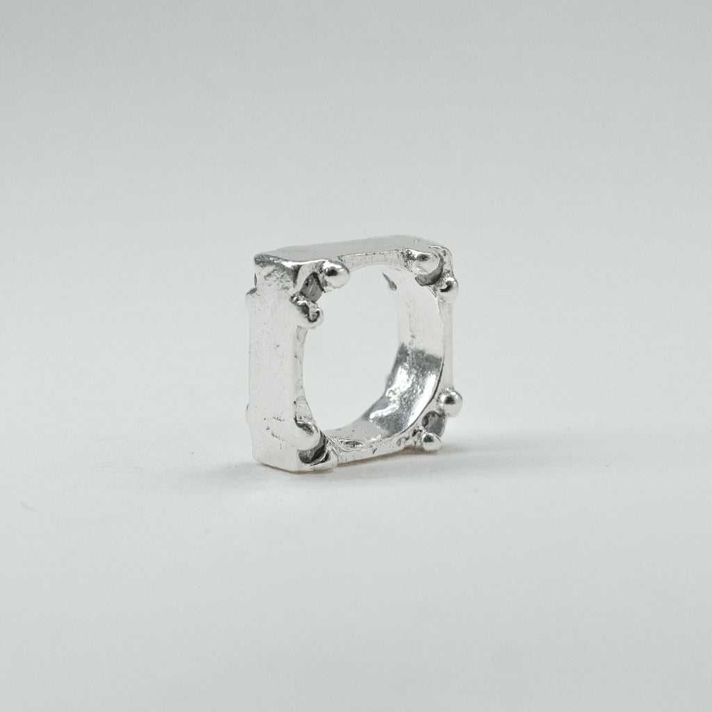 Hand-sculpted sterling silver ring with a bold, square silhouette and deep textured finish, featuring small round gemstones set into each corner.
