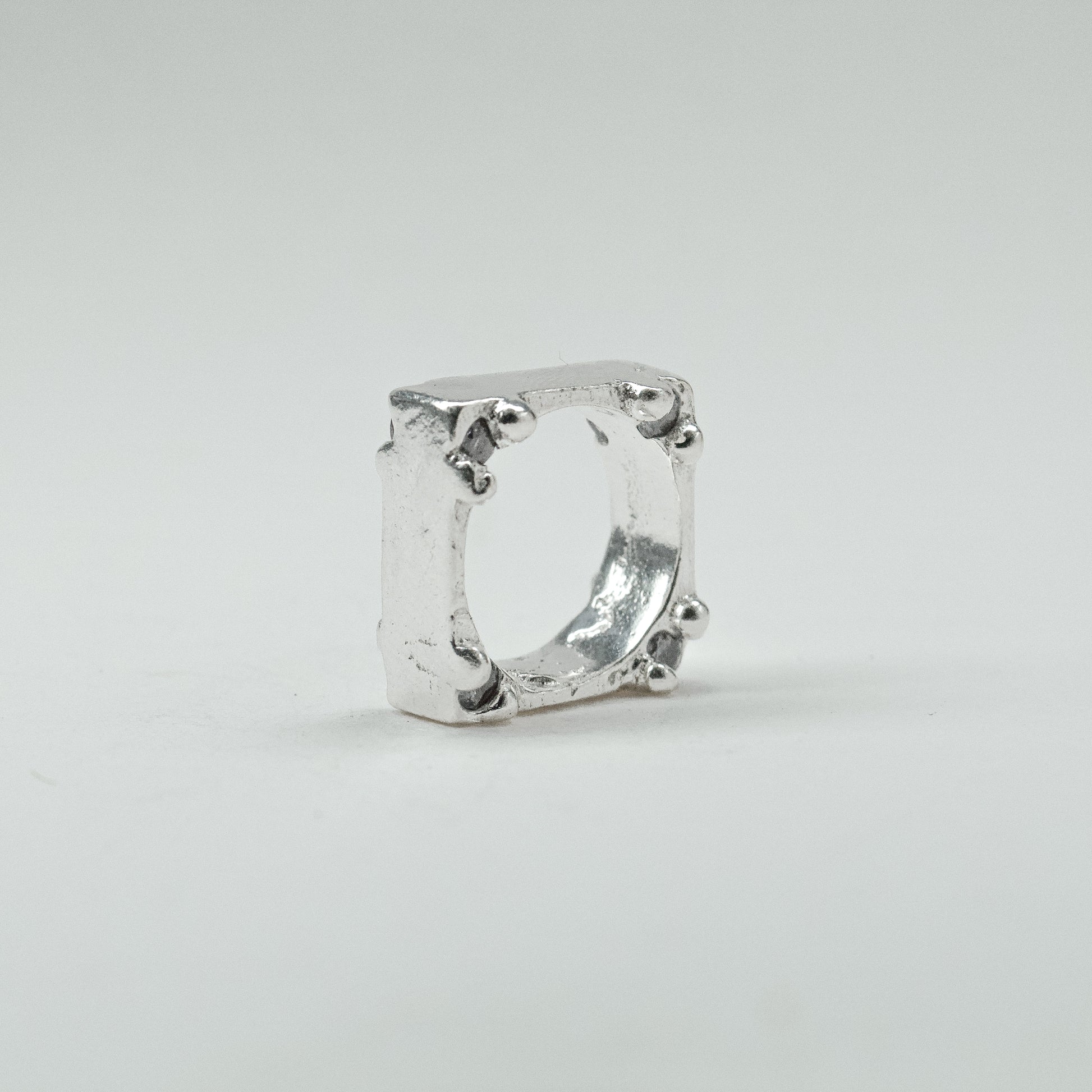 Hand-sculpted sterling silver ring with a bold, square silhouette and deep textured finish, featuring small round gemstones set into each corner.
